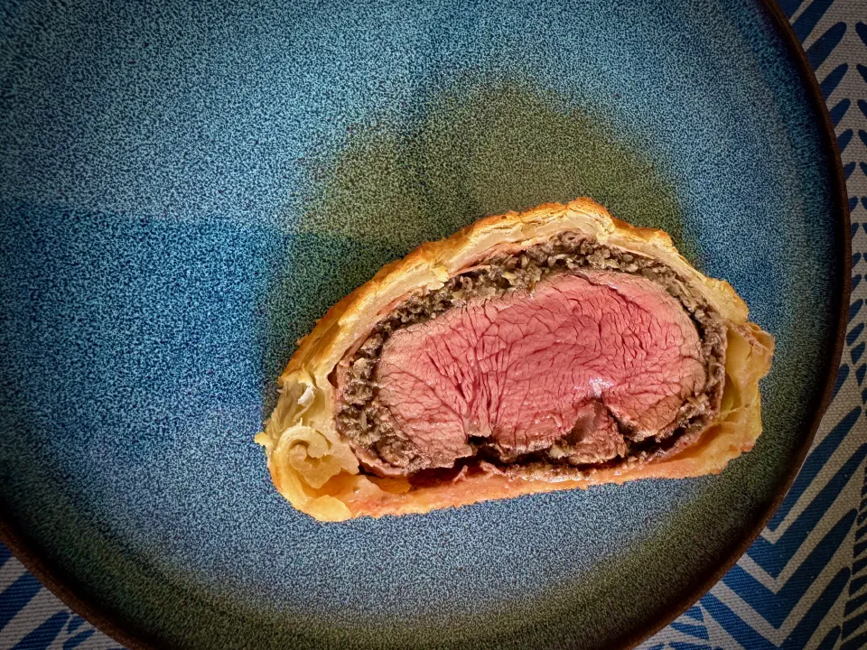 The finished Beef Wellington, sliced to reveal a ruby-pink fillet ringed with dark mushroom duxelles and golden pastry